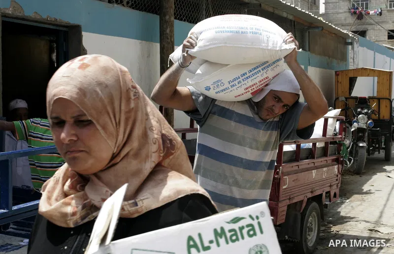 A Palestinian man carries a bag with wheat flour on his shoulders as others receive food aids from the United Nations Relief and Works Agency (UNRWA) at the Rafah refugee camp, in the southern Gaza Strip on August 15, 20...