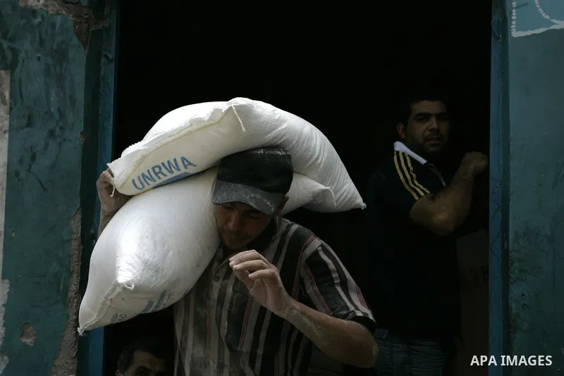 A Palestinian man carries a bag with wheat flour on his shoulders as others receive food aids from the United Nations Relief and Works Agency (UNRWA) at the Rafah refugee camp, in the southern Gaza Strip on August 15, 20...
