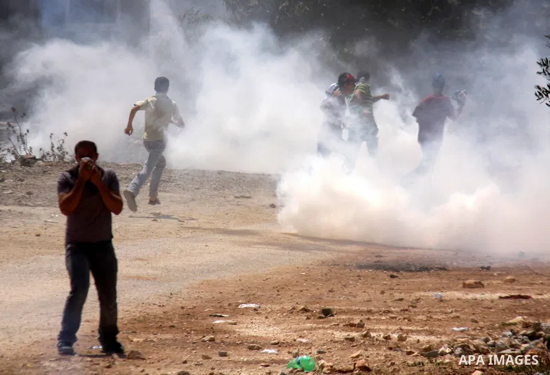 Palestinian demonstrators run as Israeli forces start to fire tear gas during clashes following a protest against the closure of a road during the second Intifada by Jewish settlers from the nearby settlement of Kadumim...