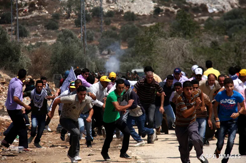 Palestinian demonstrators run as Israeli forces start to fire tear gas during clashes following a protest against the closure of a road during the second Intifada by Jewish settlers from the nearby settlement of Kadumim...