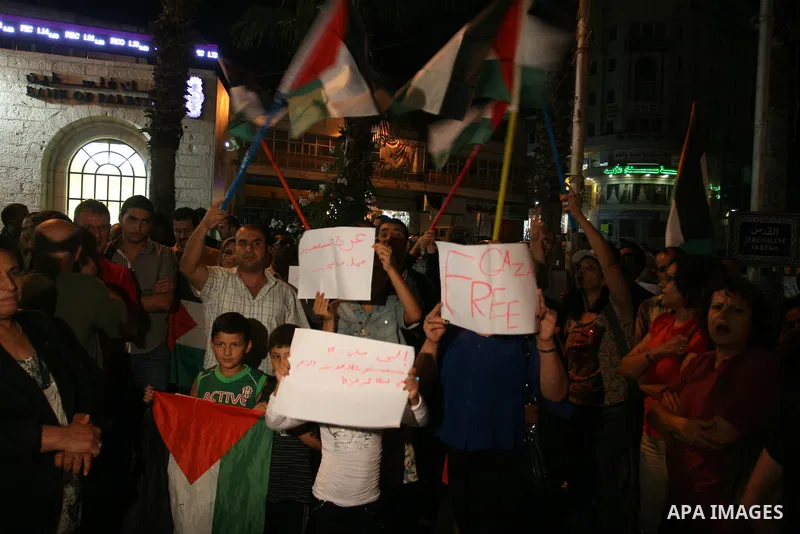 Palestinians wave with their national flag and hold placards during a protest in solidarity with the people in Gaza Strip, in the West Bank city of Ramallah on August 19,2011. Israel struck Gaza with two days of air stri...