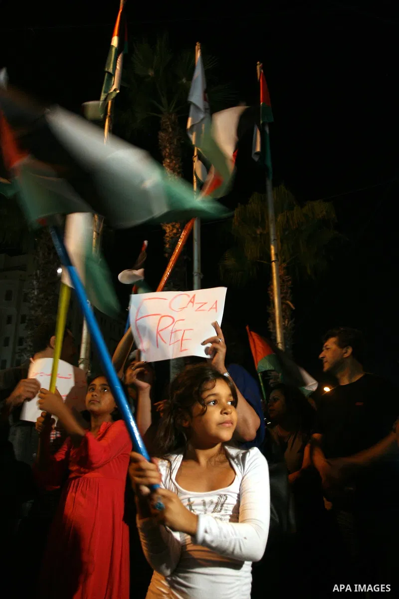 Palestinians wave with their national flag and hold placards during a protest in solidarity with the people in Gaza Strip, in the West Bank city of Ramallah on August 19,2011. Israel struck Gaza with two days of air stri...