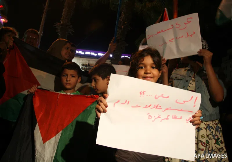 Palestinians wave with their national flag and hold placards during a protest in solidarity with the people in Gaza Strip, in the West Bank city of Ramallah on August 19,2011. Israel struck Gaza with two days of air stri...