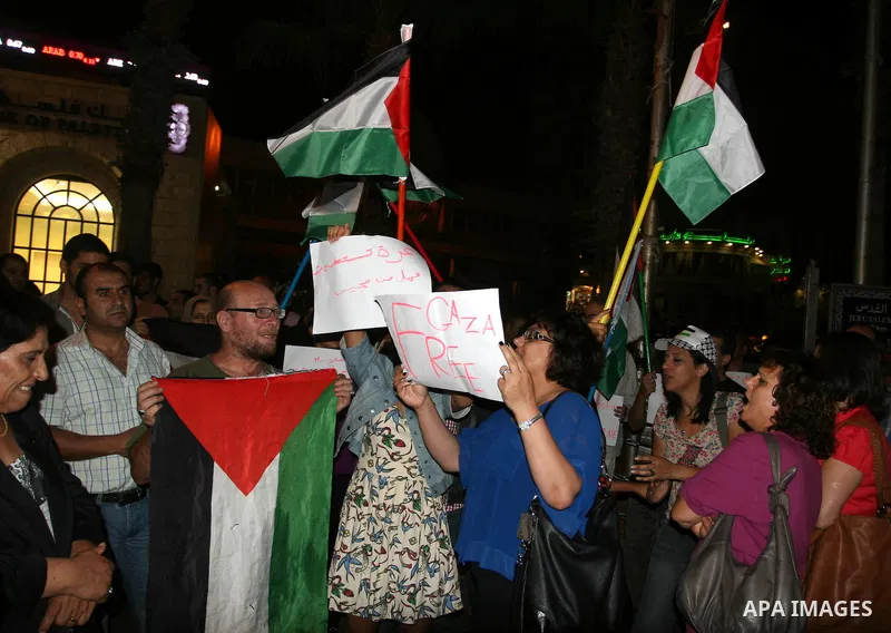 Palestinians wave with their national flag and hold placards during a protest in solidarity with the people in Gaza Strip, in the West Bank city of Ramallah on August 19,2011. Israel struck Gaza with two days of air stri...