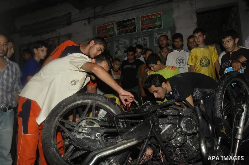 Palestinians inspect a destroyed motorcycle following an Israeli airstrike killing three Palestinian who were riding it, at the main road in Gaza City, Friday, Aug. 19, 2011. Palestinian official said that Dr. Monzer Qra...