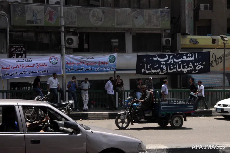 Egyptians pass under an Arabic banner with the phrase "People demand to expel the Israeli ambassador" near the Israeli embassy in Cairo, Egypt, Sunday, Aug. 21, 2011. Hundreds of Egyptians protest the deaths of Egyptian...
