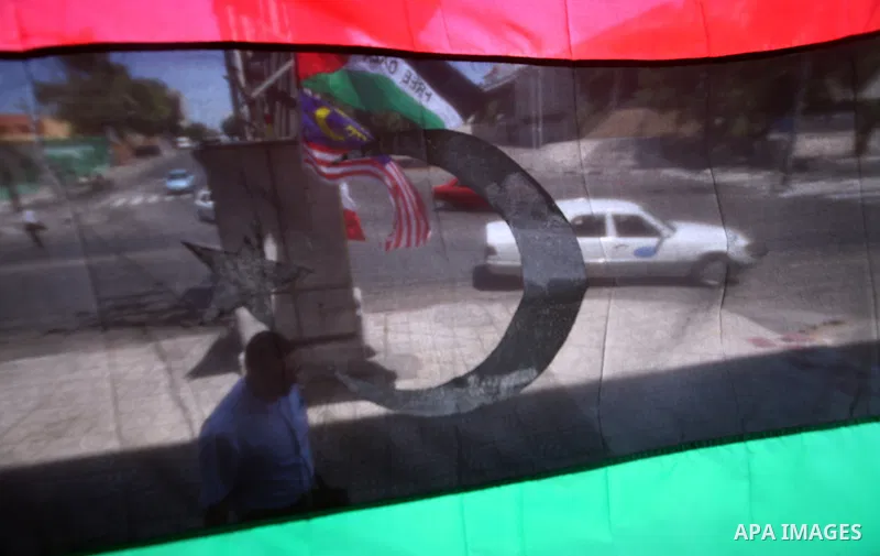 Palestinian people walk past a Libyan rebel flag in front of a shop in Gaza City, on August 24, 2011. The Hamas government and Palestinian liberation movements are reportedly showing solidarity with Libya after Libyan re...