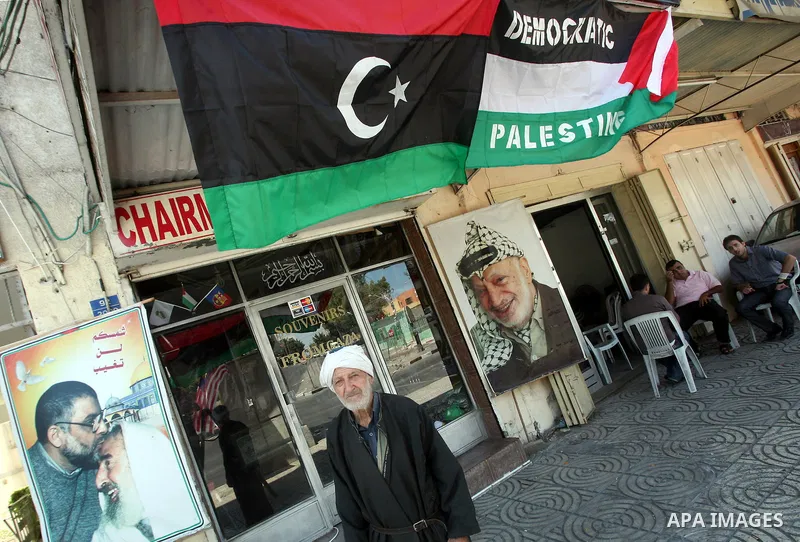 Palestinian people walk past a Libyan rebel flag in front of a shop in Gaza City, on August 24, 2011. The Hamas government and Palestinian liberation movements are reportedly showing solidarity with Libya after Libyan re...