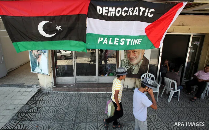 Palestinian people walk past a Libyan rebel flag in front of a shop in Gaza City, on August 24, 2011. The Hamas government and Palestinian liberation movements are reportedly showing solidarity with Libya after Libyan re...