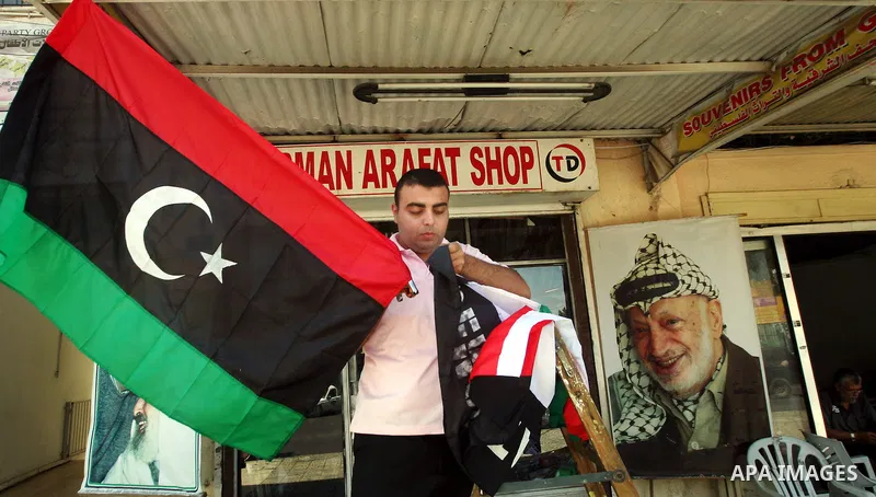 Palestinian merchant Tarek Abu Dayya hangs up a Libyan rebel flag in front of his shop in Gaza City on August 24, 2011. The Hamas government and Palestinian liberation movements are reportedly showing solidarity with Lib...