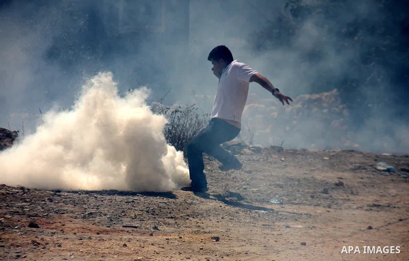 A Palestinian youth tries to seek cover from tear gas in clashes with Israeli troops during the weekly protest against the settlement of Qadomim, near the village of Kofr Qadom, west of Nablus City, in the Israeli-occupi...