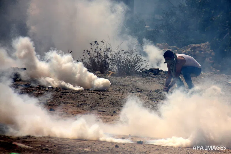 A Palestinian youth tries to seek cover from tear gas in clashes with Israeli troops during the weekly protest against the settlement of Qadomim, near the village of Kofr Qadom, west of Nablus City, in the Israeli-occupi...