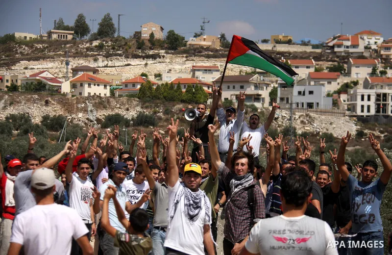 Palestinian demonstrators wave their national flag and chant slogans as they protest against the closure of a road during the second Intifada (uprising) by Jewish settlers from the nearby settlement of Kadumim (backgroun...