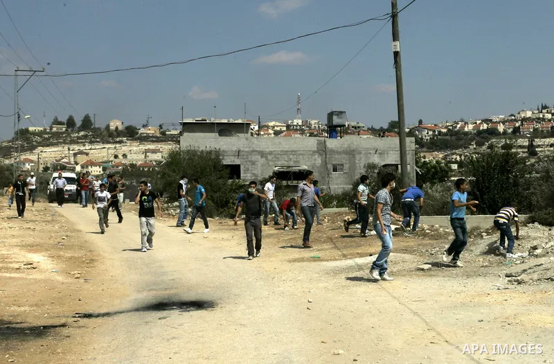 Palestinian demonstrators throw stones toward Israeli soldiers during a protest against the closure of a road during the second Intifada (uprising) by Jewish settlers from the nearby settlement of Kadumim (background), o...