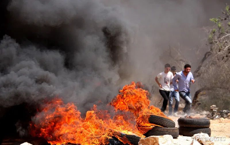 Palestinian demonstrators pass burning tires as they protest against the closure of a road during the second Intifada (uprising) by Jewish settlers from the nearby settlement of Kadumim, on September 2, 2011 in the West...