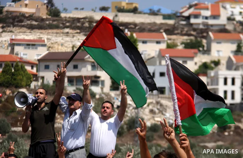 Palestinian demonstrators wave their national flag and chant slogans as they protest against the closure of a road during the second Intifada (uprising) by Jewish settlers from the nearby settlement of Kadumim (backgroun...