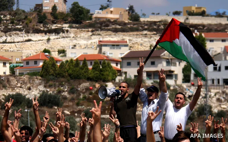 Palestinian demonstrators wave their national flag and chant slogans as they protest against the closure of a road during the second Intifada (uprising) by Jewish settlers from the nearby settlement of Kadumim (backgroun...