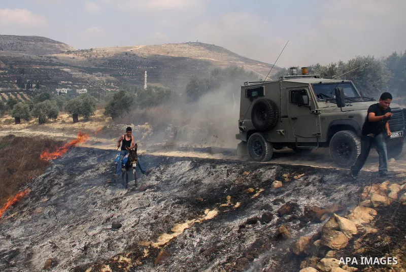 A Palestinian man rides a donkey past an Israeli military jeep as villagers try to extinguish fires in a olive grove and fields which according to the local Palestinian villagers was started by settlers from a near by Je...