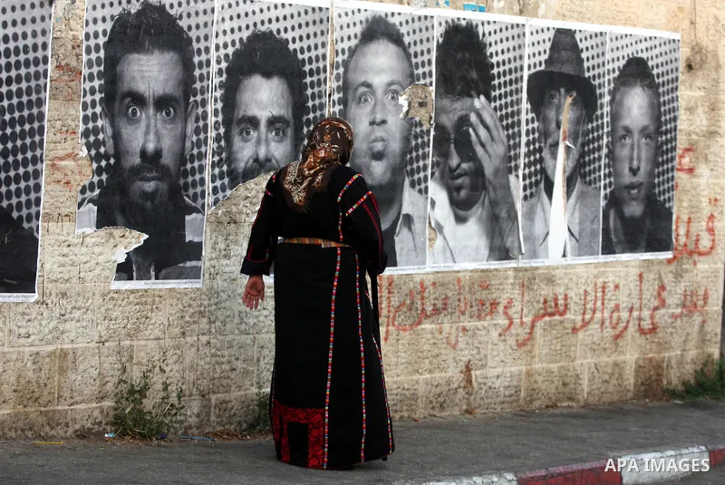 A Palestinian woman walks past large black and white photographs taken by French street artist JR of Palestinians, on September 6, 2011, in the West Bank city of Ramallah. JR's project entails having Palestinian and Isra...