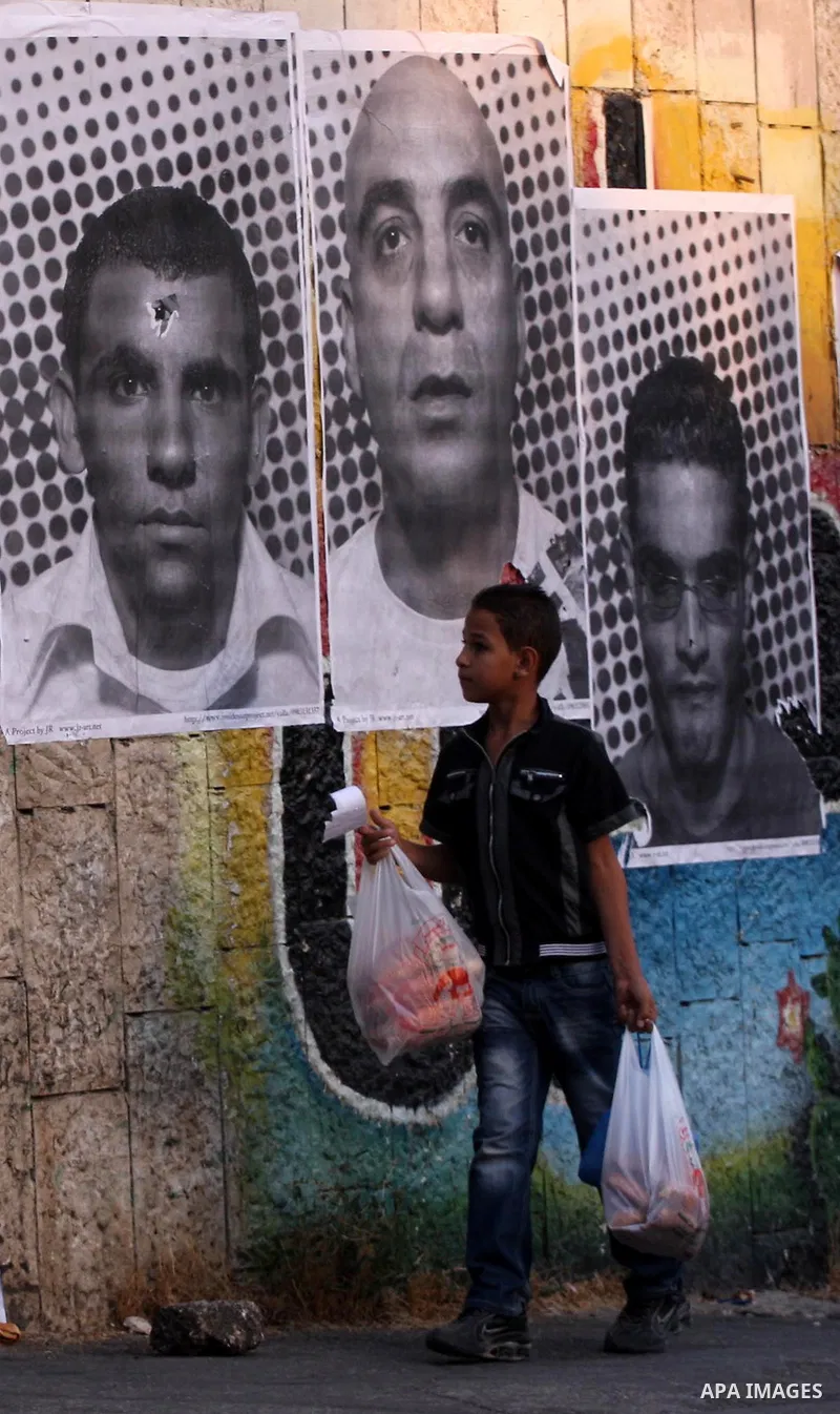 A Palestinian boy walks past large black and white photographs taken by French street artist JR of Palestinians, on September 6, 2011, in the West Bank city of Ramallah. JR's project entails having Palestinian and Israel...