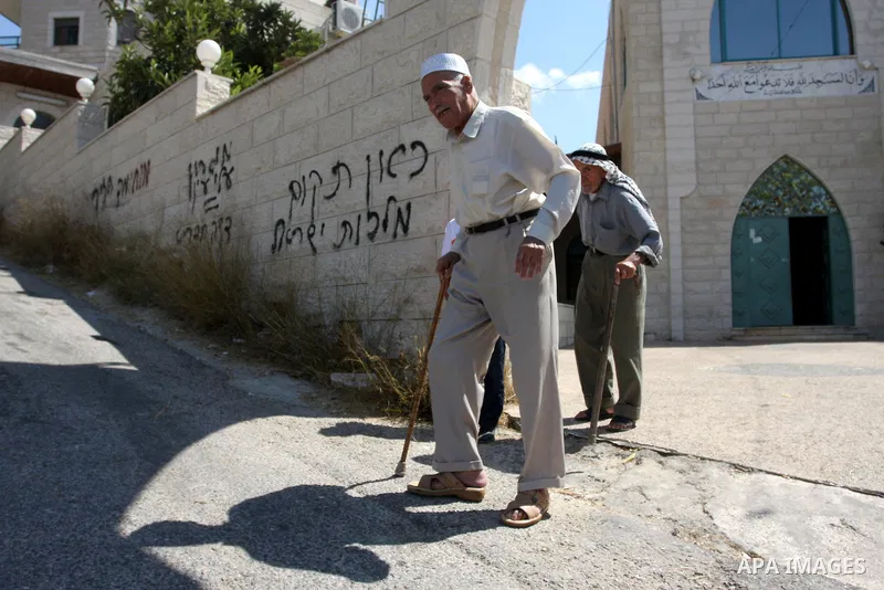 Palestinians walk past near a vandalised mosque door with the Hebrew words in the West Bank village of Birzeit near Ramallah September 9, 2011. Photo by Issam Rimawi