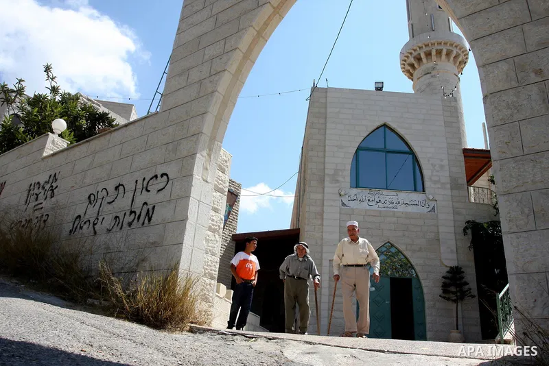Palestinians walk past near a vandalised mosque door with the Hebrew words in the West Bank village of Birzeit near Ramallah September 9, 2011. Photo by Issam Rimawi