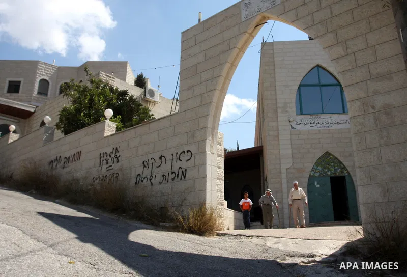 Palestinians walk past near a vandalised mosque door with the Hebrew words in the West Bank village of Birzeit near Ramallah September 9, 2011. Photo by Issam Rimawi