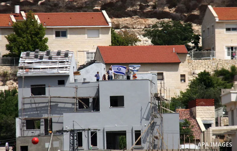 Isralei settlers from settlement of Qadomim wave Israeli flags as they watch Palestinian protesters from a rooftop, during the weekly protest against the settlement of Qadomim, near the village of Kofr Qadom, west of Nab...