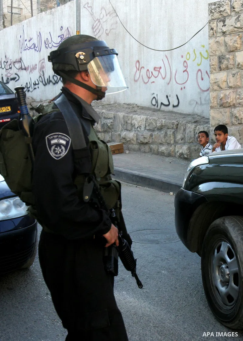 Palestinian children sit past Israeli riot policeman standing guard in the east Jerusalem neighborhood of Silwan on Sep. 13, 2011 following brief clashes between police and Palestinian stone throwers. Photo by Mahfouz Ab...