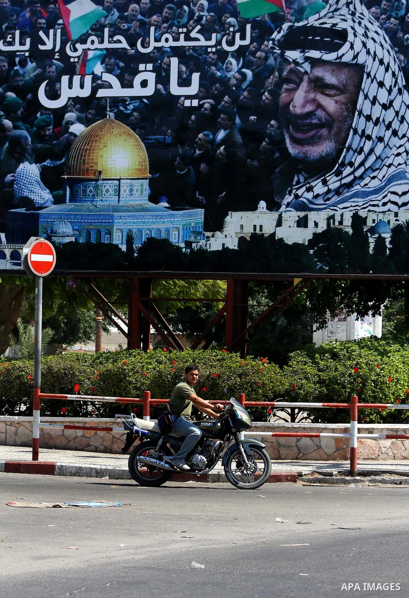 A Palestinian man rides his bicycle past a billboard which bears a portait of late Palestinian leader Yasser Arafat, with the Arabic slogan: "My dream will not be compete without Jerusalem," in central Gaza City on Septe...