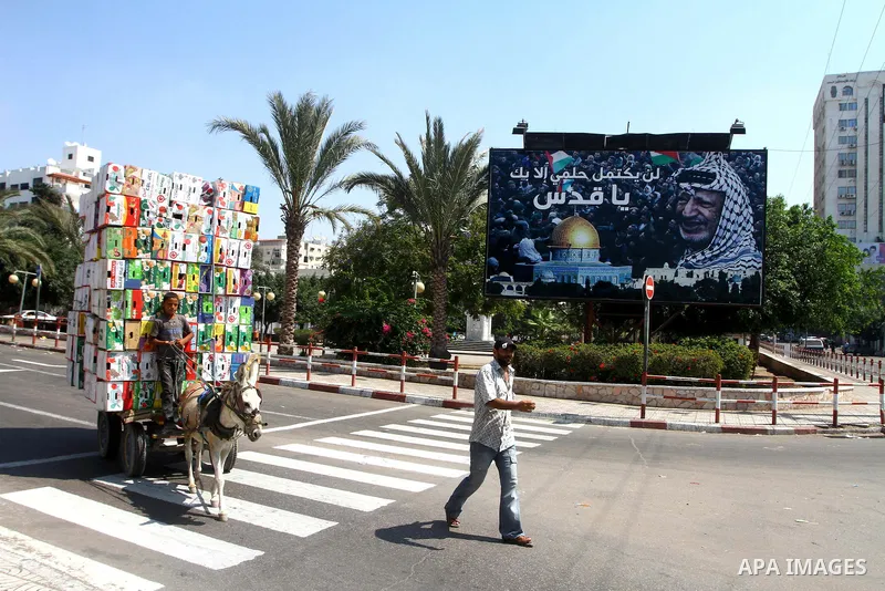 A Palestinian boy rides his donkey cart past a billboard which bears a portait of late Palestinian leader Yasser Arafat, with the Arabic slogan: "My dream will not be compete without Jerusalem," in central Gaza City on S...
