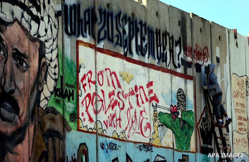 Foreign activist paints graffiti on a separation barrier during a protest calling for a Palestinian state with full UN membership at the Qalandia checkpoint between the West Bank city of Ramallah and Jerusalem, Saturday,...