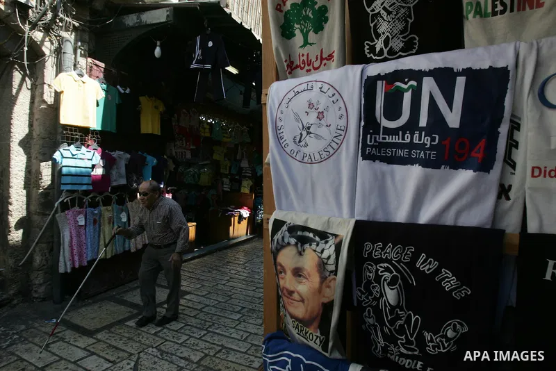 Palestinians walk past a souvenir shop in Jerusalem's Old City displaying T-shirts with pictures of French President Nicolas Sarkozy wearing the traditional Arab headdress keffiyeh, as a group of Jews touring a Jerusalem...