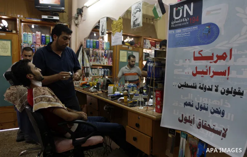 A Palestinian hairdresser cuts customer's hair near a poster of support of the UN bid for palestinian statehood, in the southern Gaza Strip Rafah refugee camp on September 18, 2011. The Islamist Hamas movement said the U...