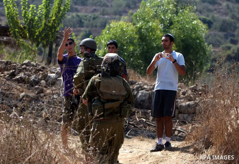 Israeli soldiers watch over armed Jewish settlers from the Halamish settlement near members of pro-Palestinian volunteer-based campaign which will intervene and respond to cases of violence towards Palestinians by Jewish...