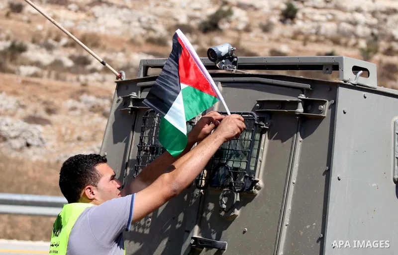 A Palestinian man places his national flag on an army jeep during the launch of pro-Palestinian volunteer-based campaign which will intervene and respond to cases of violence towards Palestinians by Jewish settlers in th...