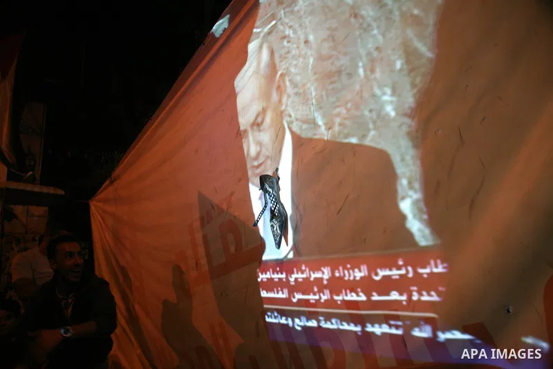Palestinians hold up shoes as they watch a screen relaying live footage of Israeli Prime Minister Benjamin Netanyahu speech at the United Nations General Assembly in New York on September 23, 2011 in the West Bank city o...