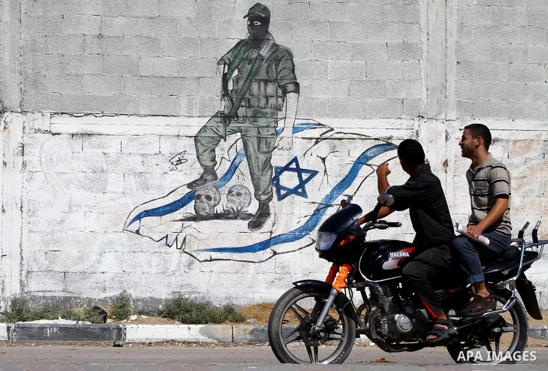 Palestinians ride motorcycle past a graffiti depicting a Palestinian militant stepping on skulls and the Israeli flag in Gaza City, Saturday, Sept. 28, 2011 as Palestinians mark the 11th anniversary of Al-Aqsa Intifada (...