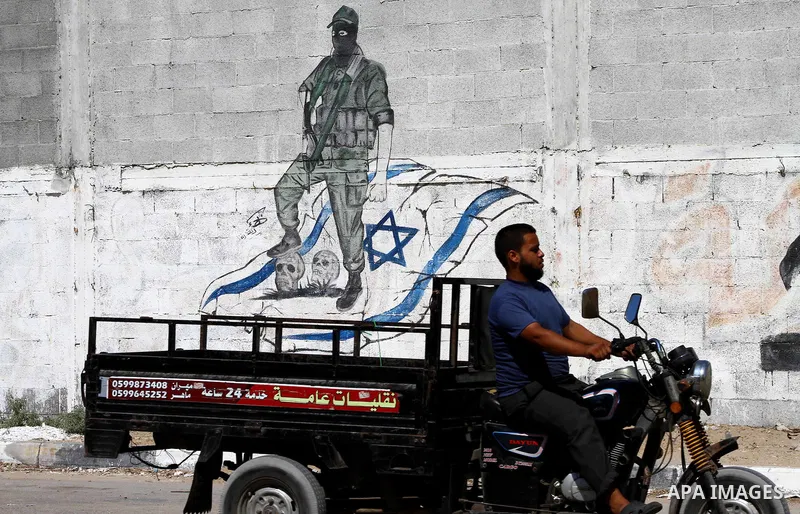 Palestinians ride motorcycle past a graffiti depicting a Palestinian militant stepping on skulls and the Israeli flag in Gaza City, Saturday, Sept. 28, 2011 as Palestinians mark the 11th anniversary of Al-Aqsa Intifada (...
