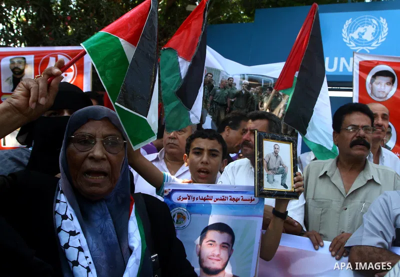 Palestinians hold the Palestinian flag and pictures of relatives held in Israeli jails, during a protest calling for their release, in front of the International UNSCO headquarters in Gaza City, on Sept. 29, 2011. Photo...