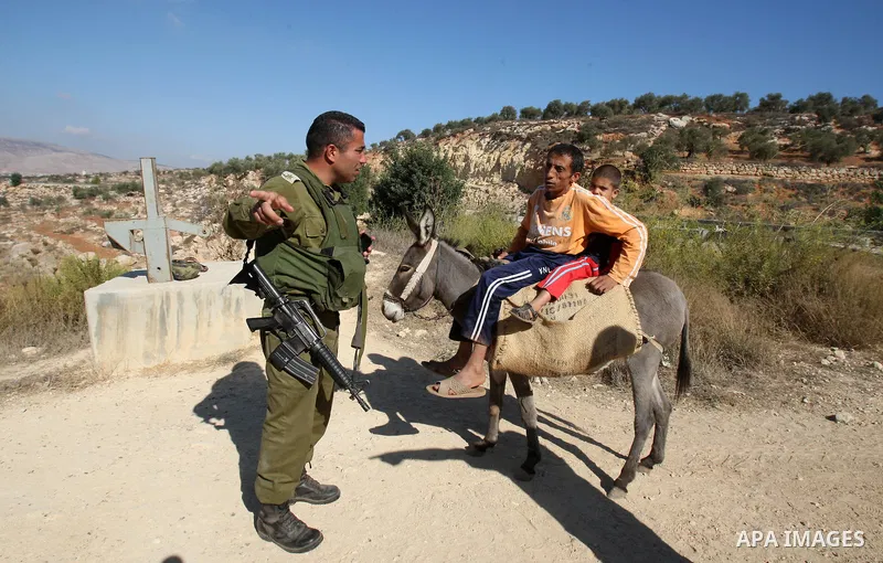 An Israeli soldier stands guard at a barrier erected on Palestinian land to protect nearby Jewish settlements in the occupied West Bank, as Palestinian farmers cross to harvest their olive groves just outside the Palesti...