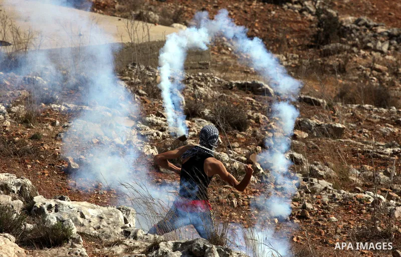 A Palestinian youth uses a sling to hurl tear gas canister towards Israeli soldiers during a weekly demonstration against Israeli settlement expansion, in the West Bank village of Nabi Saleh, on October 7, 2011. Photo by...