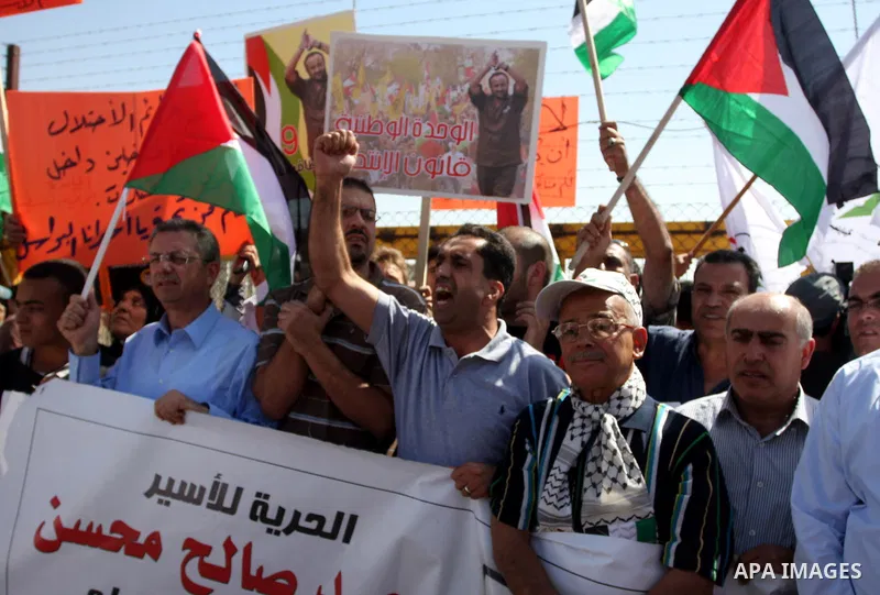 Palestinian protestors hold banners and wave national flag during a demonstration calling for the release of prisoners held in Israeli jails and in support of inmates in hunger strike, on October 11, 2011 near Israel's O...