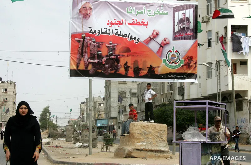 Palestinians walk next to a poster for captured Israeli soldier Gilad Shalit in Rafah town in the southern Gaza Strip October 12, 2011. Israelis welcomed on Wednesday a major prisoner swap that will free soldier Gilad Sh...
