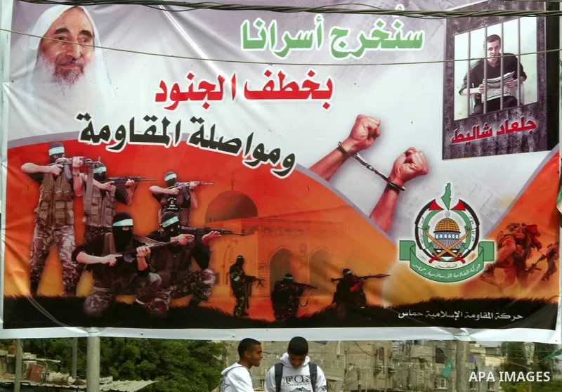 Palestinians walk next to a poster for captured Israeli soldier Gilad Shalit in Rafah town in the southern Gaza Strip October 12, 2011. Israelis welcomed on Wednesday a major prisoner swap that will free soldier Gilad Sh...