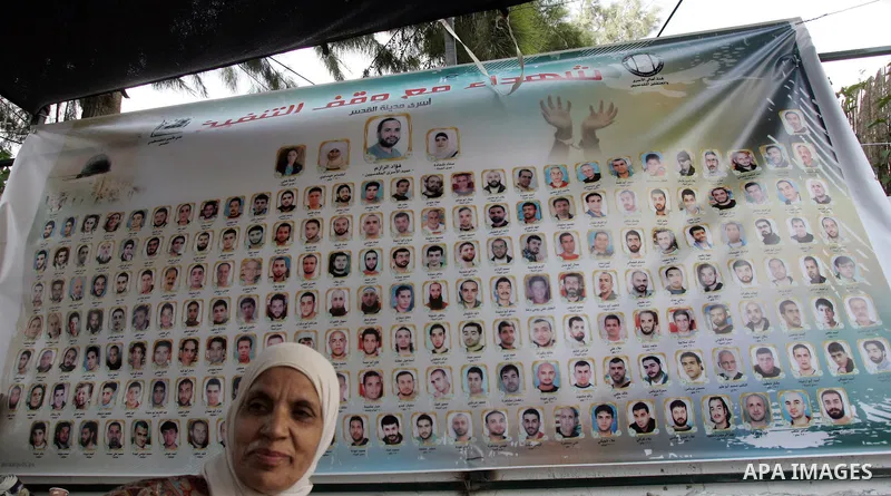 Palestinians sit below the images of prisoners who may be released later this week. A large sign hangs at the headquarters of the Red Cross in East Jerusalem with images of prisoners who will be freed by the recent excha...