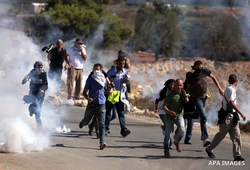 Palestinian, Israeli and foreign activists run away from tear gas canisters fired by Israeli troops during a demonstration against the expansion of the nearby Jewish settlement of Halamish in the West Bank village of Nab...