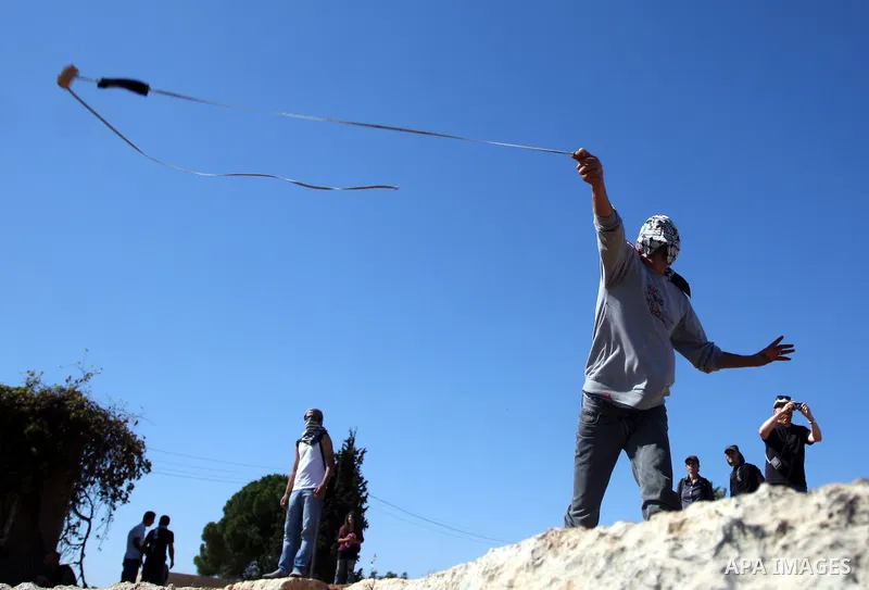 A masked Palestinian demonstrator wields a sling-shot at Israeli troops during a demonstration against the expansion of the nearby Jewish settlement of Halamish in the West Bank village of Nabi Saleh, near Ramallah, Frid...