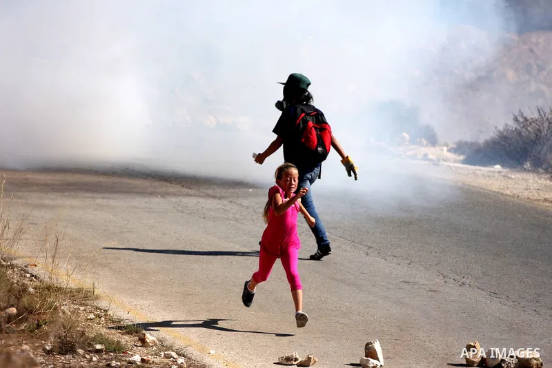 A Palestinian girl runs away from tear gas canisters fired by Israeli troops during a demonstration against the expansion of the nearby Jewish settlement of Halamish in the West Bank village of Nabi Saleh, near Ramallah,...