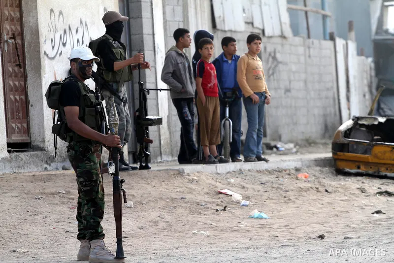 Palestinian boys keep watch as armed Hamas militants stand guard at a street in Gaza city on October 18, 2011 as an Israeli-Palestinian prisoner swap deal gets under way. Buses carrying 477 Palestinian prisoners were hea...
